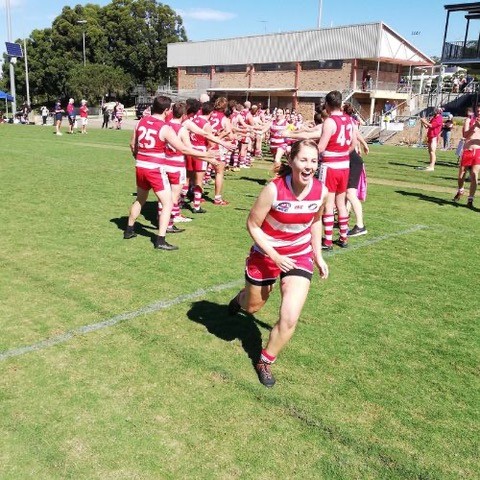 Two lines of people, dressed in Aussie rules football shorts and guernseys, form a welcome guard for players running onto a sporting field.