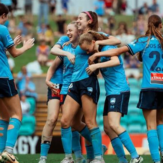 Players from a women's football (soccer) team gathering on the field in celebration.