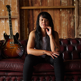 A woman sitting on a brown couch with her red guitar