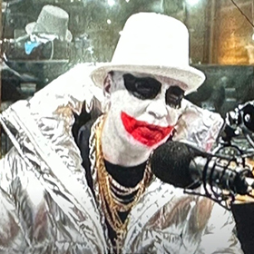 A man in a clown outfit talking into a microphone