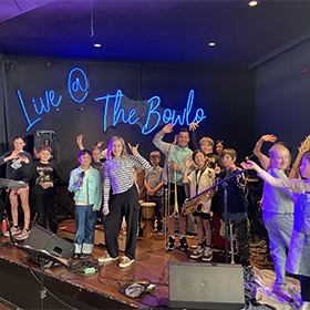 a group of kids on stage in front of a neon sign