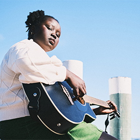 A woman playing a guitar against a blue sky