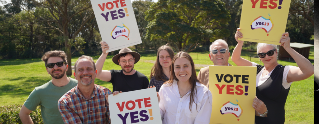 Group of smiling people holding Yes placards