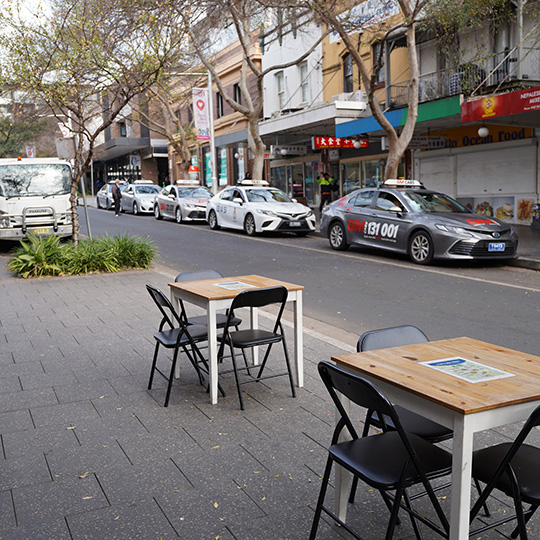 Tables on a street with green plants in the background