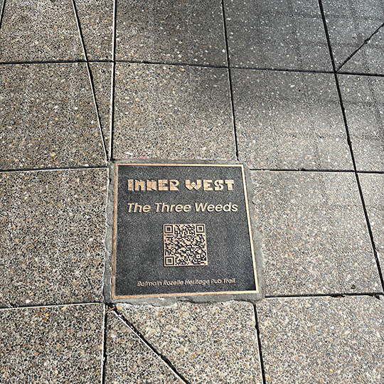 A bronze footpath plaque with a QR code reads "Three Weeds Hotel"