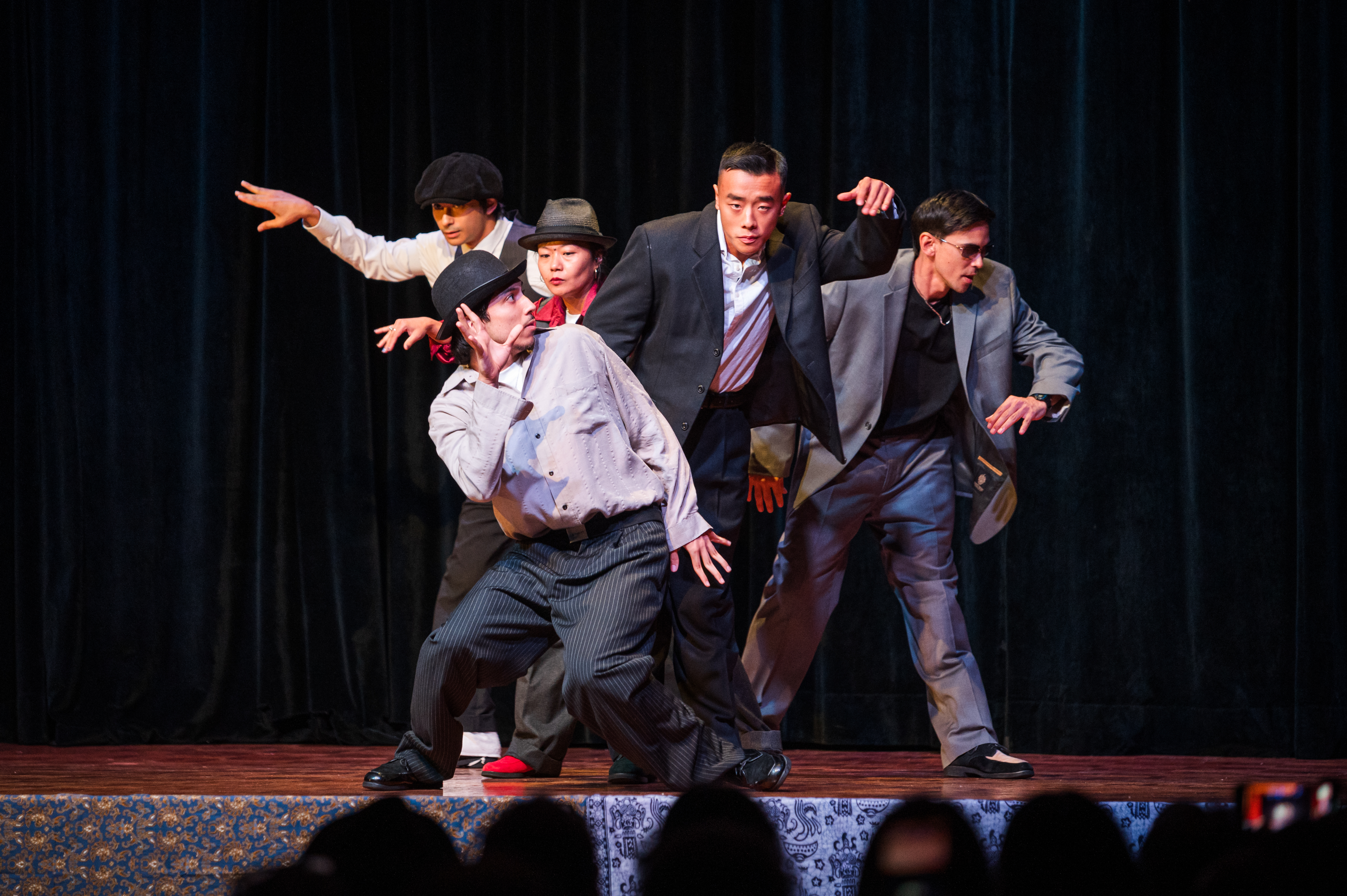 Five performers on stage in business wear mid pose street style dancing