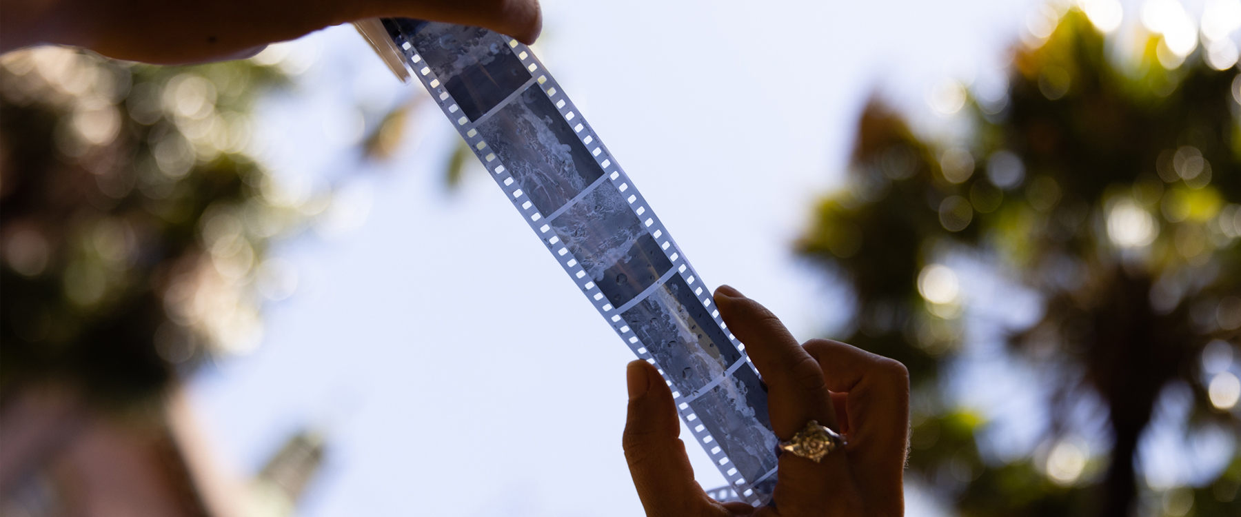 Photo of a photography negative strip held up to the sky by a person wearing gold rings