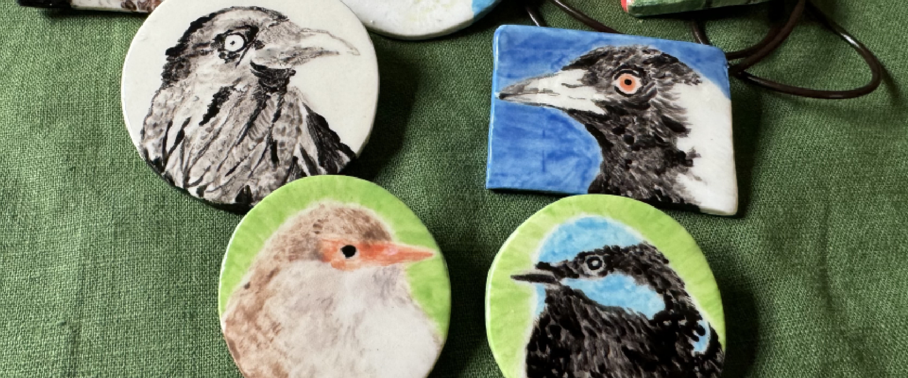 photo of four ceramic round brooches with birds on them, there is a green tablecloth in the background