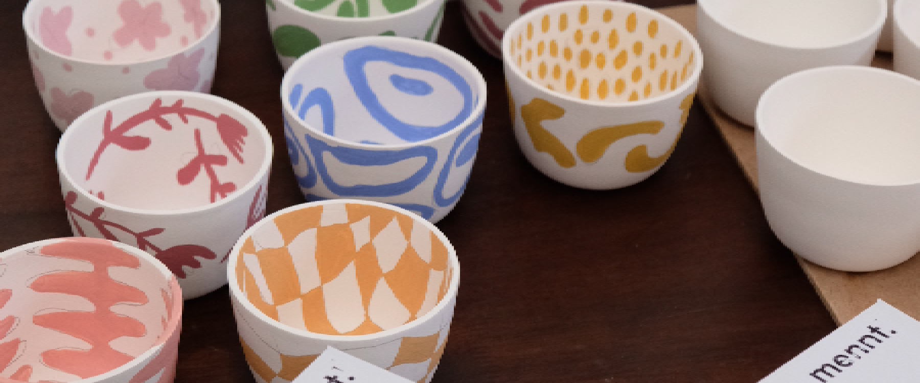 Photo of many little cermic bowls with organic shapes, checks, plants, circles, some branding mennt can be seen on a display box