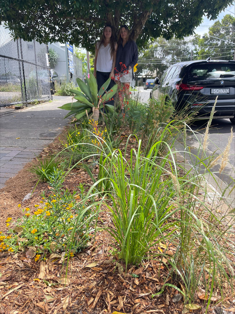 Two people stnading in the shade of a tree surrounded by a verge garden.