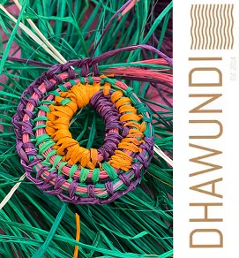 Photo of a woven circular shape made with electric green, purple, pink and orange - it lies on a bed of green raffia strands