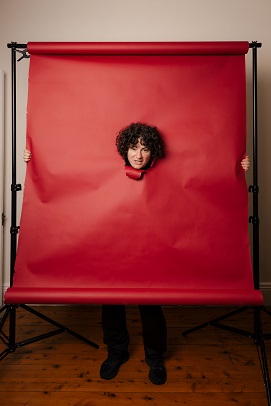 Photo of artist Prince peeking though a piece of ripped paper, the photo is black and white and only visible is their eye, nose and a fingers