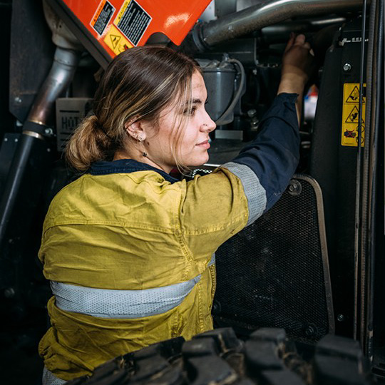 A person in workwear repairing an earthmoving vehicle