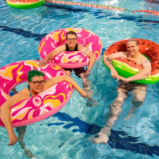 Three smiling people in colourful flotation rings in a pool