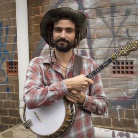 Kid Hank poses smiling, holding a banjo