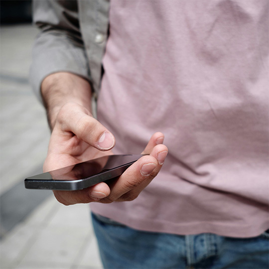 Close-up of a person's right hand holding a smartphone. Their thumb is hovering over the screen.