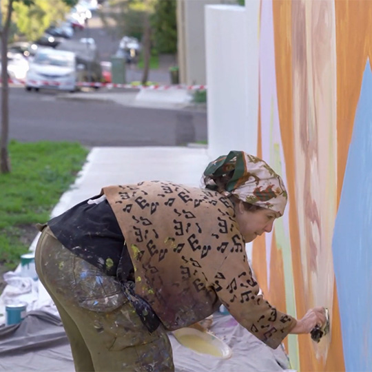 A street artist working on an artwork on the side of a building in an urban residential area.