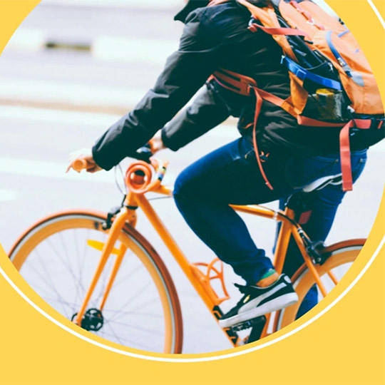 A person with a backback riding a bright orange bike on a street