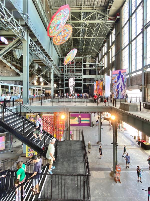 an image of insde a building with a staircase and people around with artworks around
